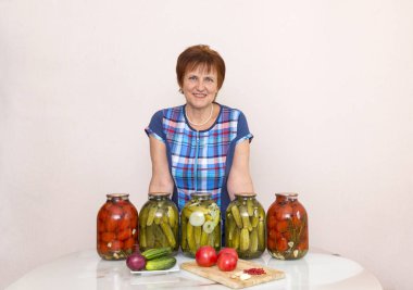 Mutfakta tablosunun yanındaki mavi ekose tunik kadında. masanın üzerine kavanoz turşu, salamura domates ve salatalık, masanın üzerine taze domates, sebze, gıda, salatalık, soğan, sarımsak, 