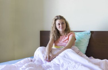 yatak ve battaniyenin altında oturan ve gülümsemek gülümseyen, Genç kadın üzerinde oturan 1 beyaz kız