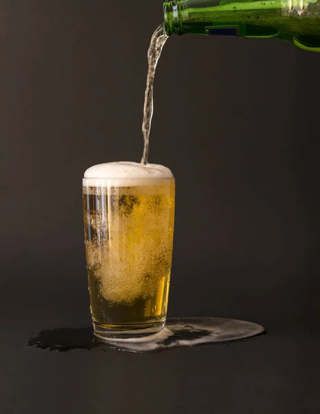 light beer is poured from a bottle into a glass on a black background, foam, bubbles