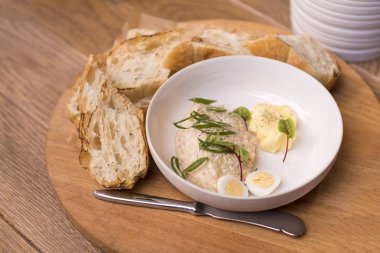 Pate adet baget ahşap tahta üzerinde beyaz bir tabakta yeşillikleri ile tavuk, bıçak, masanın üzerine snack