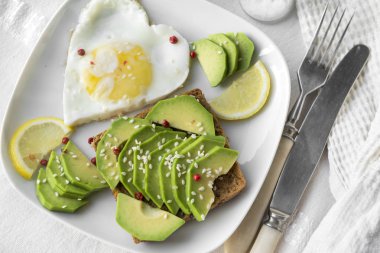 avokado, susam, sahanda yumurta, dilim limon tabak, çatal, bıçak ile sandviç