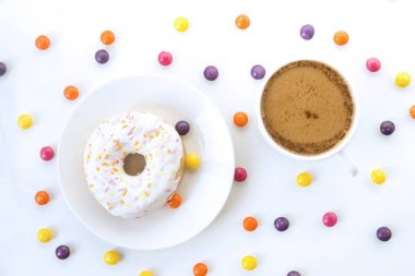 çörek bir tabak, bir fincan kahve süt, beyaz yüzey, en iyi görünüm üzerinde renkli drajelik bir sürü ile üzerine beyaz krema ile