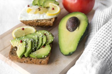 sandviç avokado dilimleri, susam ve limon, avokado yarım, yumurta, domates ile