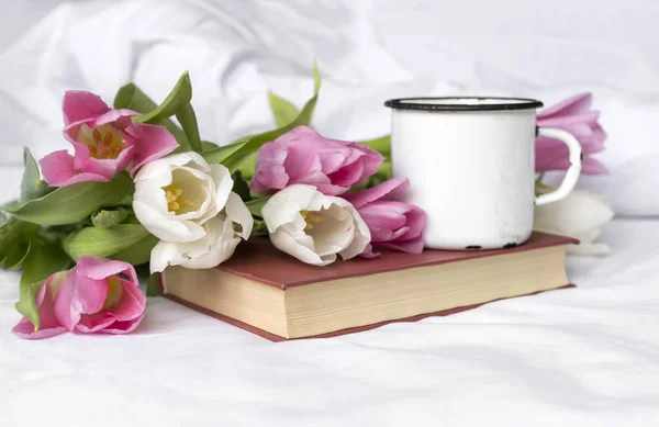 Pink and white tulips, mug on the book, white sheet — Stock Photo, Image