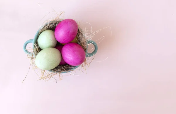 pink and green eggs in hay vtarelke top view, beige background,