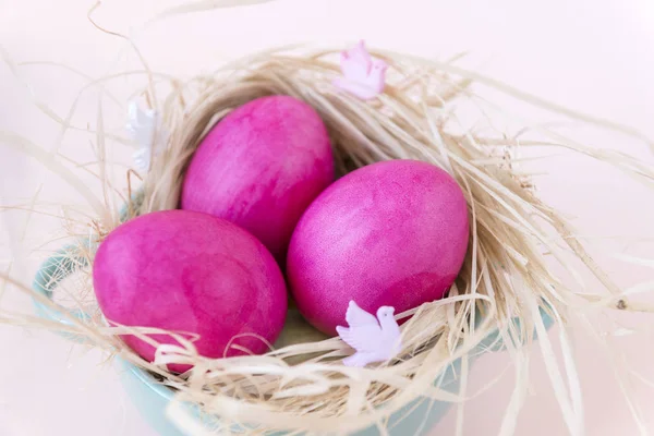 3 huevos rosados en heno en un plato sobre fondo beige — Foto de Stock