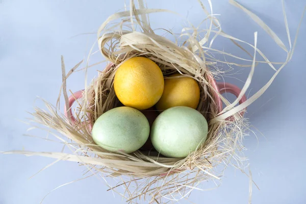 4 Huevos de Pascua en heno en un plato sobre fondo azul — Foto de Stock