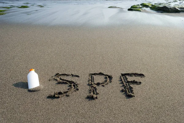 Spf 砂、ローション、海岸で白い瓶に刻まれた文字 — ストック写真
