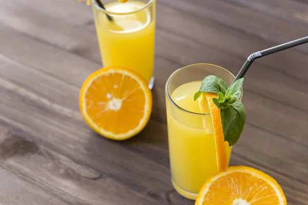 2 чашки апельсинового соку з соломою, гілочкою м'яти, половина свіжого — стокове фото