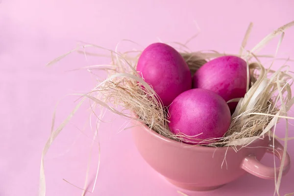 3 huevos rosados de Pascua en heno en un plato sobre un fondo rosado — Foto de Stock