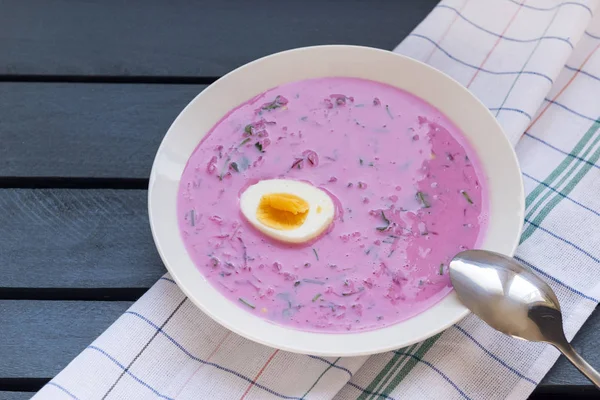 Суп из холодной свеклы с яйцом, ложкой, полотенцем на сером деревянном фоне — стоковое фото