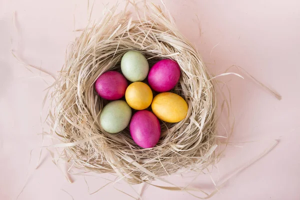 Rosa, amarillo, verde huevos de Pascua en el nido sobre fondo beige, a — Foto de Stock