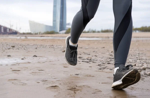 women\'s feet in dark leggings and black sneakers on the sand, ru