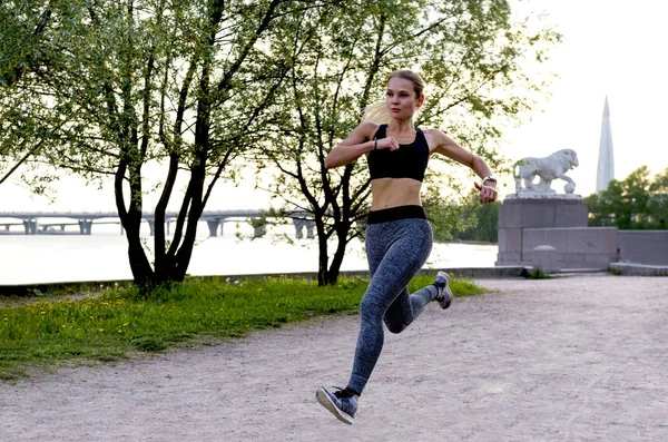 Menina esbelta em roupas esportivas corre rapidamente no parque ao longo do th — Fotografia de Stock
