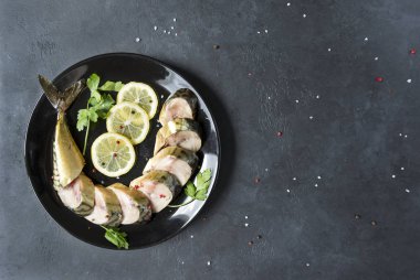 siyah bir arka planda bir plaka üzerinde parçalar halinde kesilmiş füme uskumru
