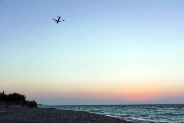 plane in the sky comes to land over the sea coast at sunset