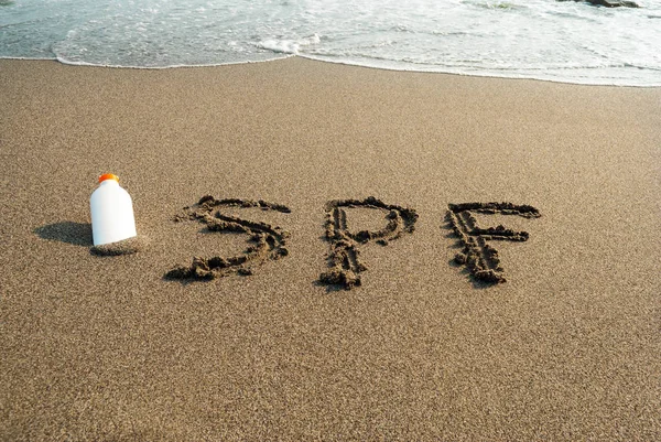 Aufschrift auf dem Sand spf, Strand, eine Flasche Sonnencreme, Sonne — Stockfoto