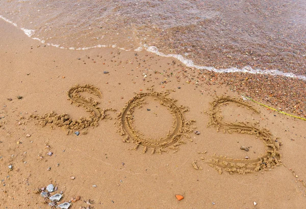 Iscrizione SOS sulla sabbia con acqua di mare — Foto Stock