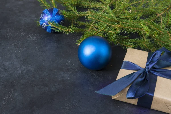 fir branches, blue balls, gift box with blue ribbon on black bac