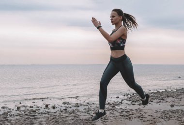 ince genç kadın gün batımında deniz kıyısında çalışır, koşucu