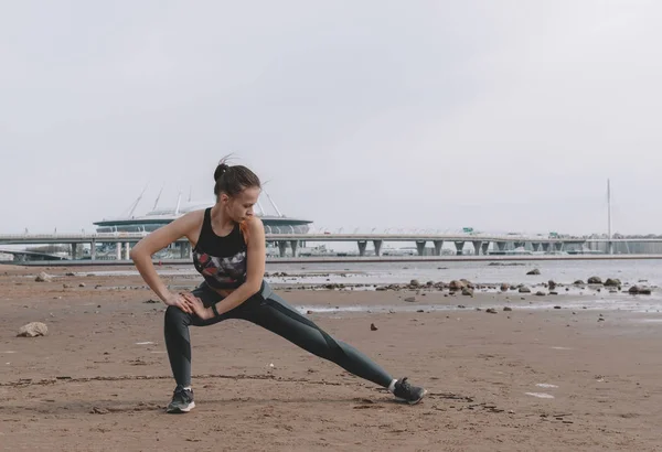 Jovem mulher esbelta em sportswear fazendo alongamento na praia — Fotografia de Stock