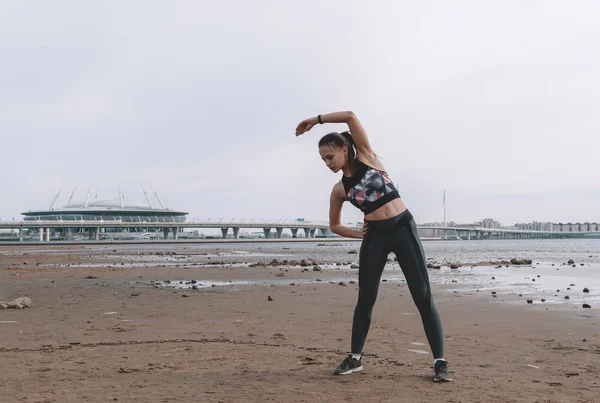 Esbelta jovem com sportswear fazendo aquecimento na praia ag — Fotografia de Stock