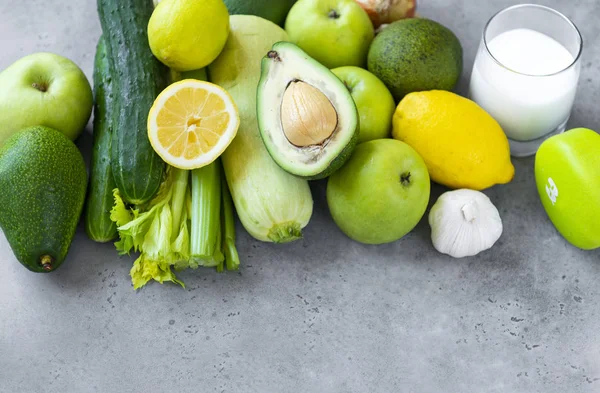 green fruits and vegetables on a gray background, glass of milk,