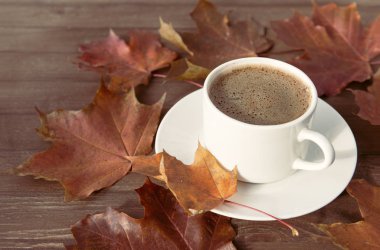 Bir fincan sade kahve, çay tabağında kırmızı sonbahar akçaağaç yapraklı.