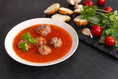 Bir tabak kırmızı domates çorbası, köfteli, sebzeli.
