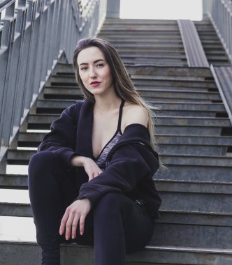 İnce, güzel, beyaz bir kadın merdivende oturuyor.