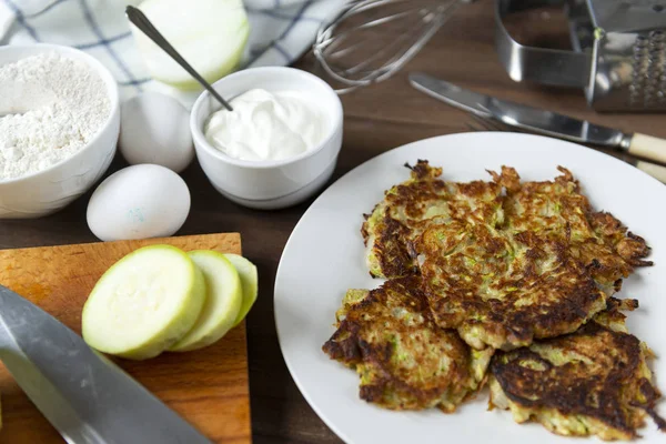 Zucchini fritters on a white plate, sour cream on a brown wooden — Stock Photo, Image