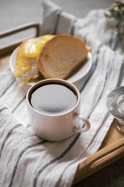 Xícara de café preto em uma bandeja, ovo e queijo sanduíche no trigo — Fotografia de Stock