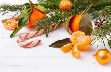 Dilimler taze mandalina, tüm mandalinalar, ladin dalları, lolipoplar, beyaz arka planda Altın Noel topu.