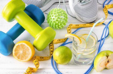 Dambıllar, limonlu bir bardak su, ölçüm bandı, ip atlama, top, spor ayakkabısı, kireç, yeşil elma, beyaz arka plan