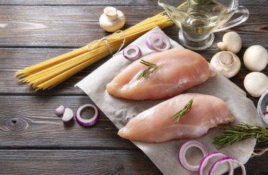 Baharatlı çiğ tavuk fileto ve makarna kesim tahtasında, tuz, yağ, biberiye, soğan, ahşap zemin üzerinde mantar,