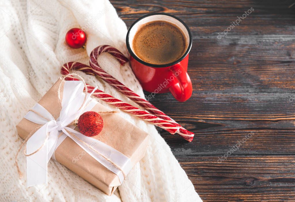1 red coffee mug, lollipops, gift box, red Christmas balls, white sweater on a brown wooden background, Christmas still life