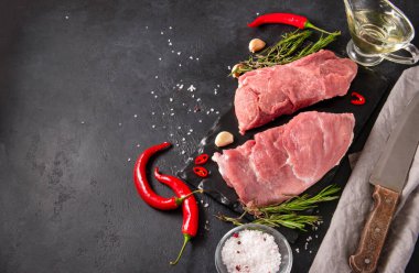 İki parça çiğ et, sarımsak, biberiye ve kırmızı biber, tuz, siyah arka planda yağ, domuz eti, bıçak, peçete.