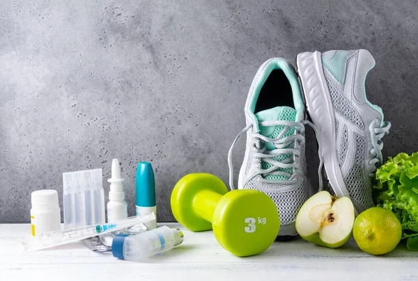 sneakers, green apples, lettuce, dumbbell,  lime, medicine, pills on a gray background, healthy lifestyle