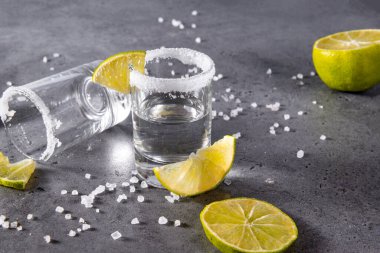 Gri arka planda tuz ve limon dilimli iki bardak tekila, güçlü bir alkollü içecek.