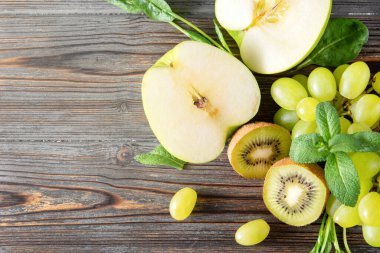Taze yeşil kivi, üzümler, elma yarımları, ahşap arka planda nane aromalı üst manzara., 