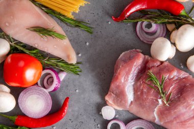 Çiğ et, tavuk fileto, domatesli domuz filetosu, soğan, biber biber, makarna, spagetti, yeşillik, biberiye, gri arka planda mantar.