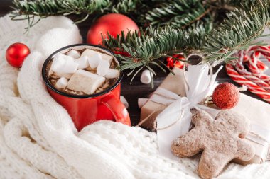 Marşmelovlu kırmızı kakao kupası, beyaz kazaklı zencefilli ekmek adam, ladin dalı, kırmızı Noel topları, Noel natürmortu