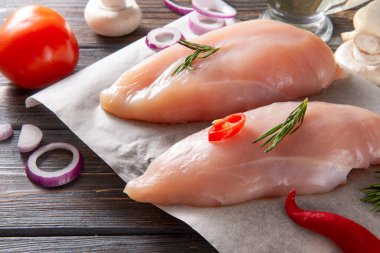 Biberiyeli çiğ tavuk filetosu, biber biberi, soğan ve domatesli ahşap zeminde parşömen.