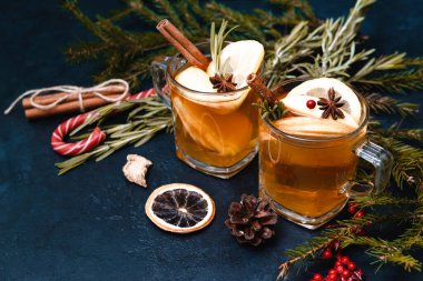 2 kupa elma dilimli meyve çayı, anason, biberiye, tarçın çubukları ve lolipoplar siyah arka planda, kış sıcak içeceği