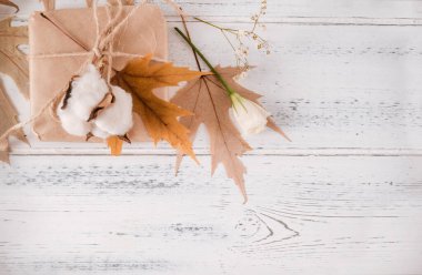 Sonbahar, hediye kutusu, düşmüş akçaağaç yaprakları, beyaz bir tahta üzerinde beyaz çiçekler ve pamuk filizi, kopyalama alanı.