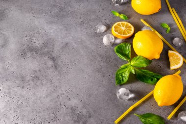 Sarı bütün limon ve dilimler, yeşil fesleğen, buz küpleri, gri arka planda sarı tüpler