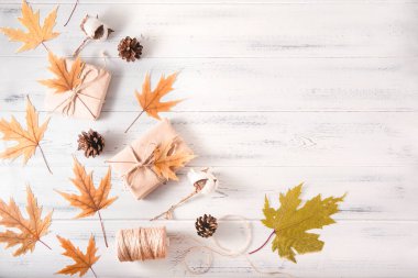 Sonbahar sarı akçaağaç yaprakları, koniler, beyaz ahşap bir arka planda iplik.