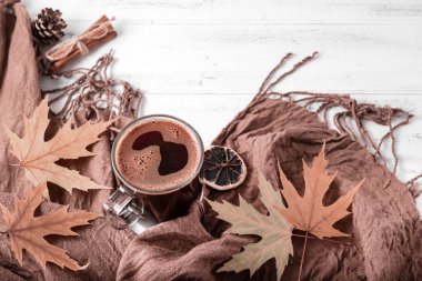 Bir fincan sade sıcak kahve, sonbahar sarısı akçaağaç yaprakları kahverengi bir eşarbın yanında, beyaz ahşap bir arka planda battaniye.