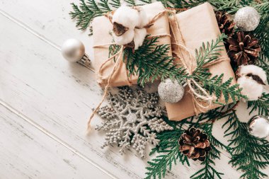 Ladin dallarında hediyeler, gümüş Noel baloları pamuk, koni, beyaz ahşap bir zeminde kar tanesi, Noel natürmortu,