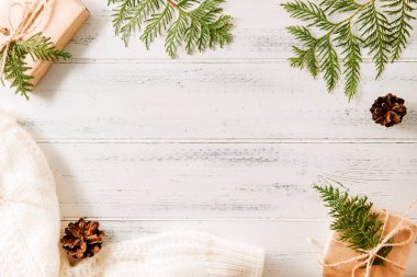 Hediye kutusu, yeşil thuja dalları, köknar dalları, kozalaklar, beyaz örgü süveter beyaz ahşap arka planda, kozalaklı dallar